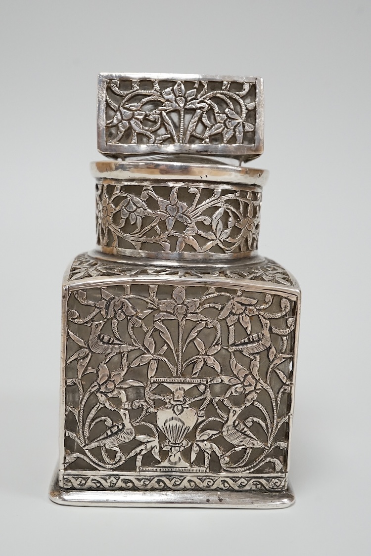 A Persian pierced white metal overlaid moulded glass salts bottle with stopper, decorated with urns and birds amid scrolling foliage, overall height 94mm.